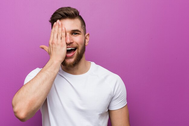 Young handsome caucasian man having fun covering half of face with palm.