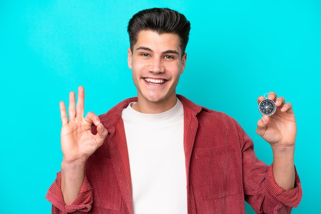 Young handsome caucasian man holding compass showing ok sign with fingers