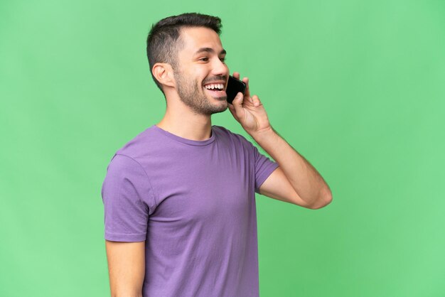 Young handsome caucasian man over isolated background keeping a conversation with the mobile phone