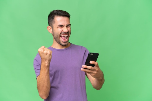 Young handsome caucasian man over isolated background with phone in victory position