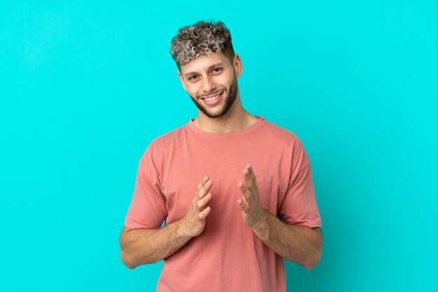 Young handsome caucasian man isolated on blue background applauding after presentation in a conference