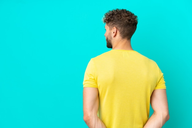 Young handsome caucasian man isolated on blue background in back position and looking back