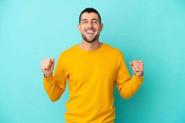 Young handsome caucasian man isolated on blue background celebrating a victory in winner position