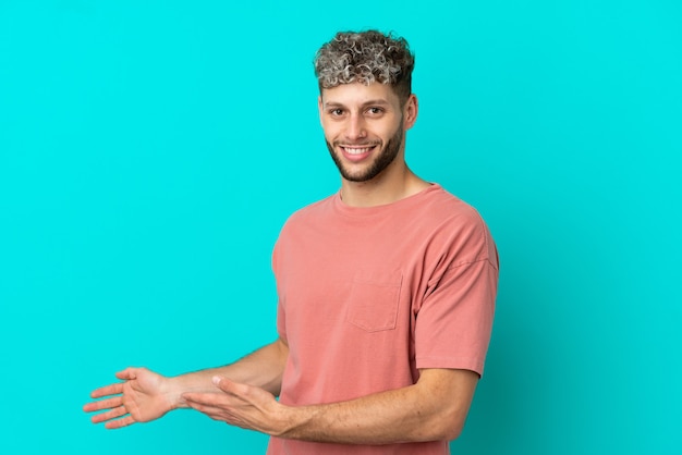 Young handsome caucasian man isolated on blue background extending hands to the side for inviting to come