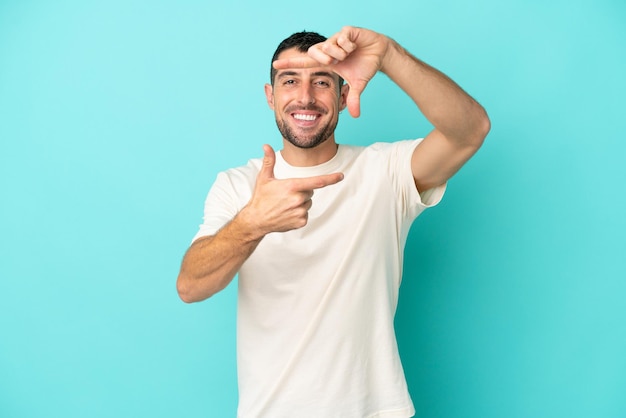 Young handsome caucasian man isolated on blue background focusing face. framing symbol