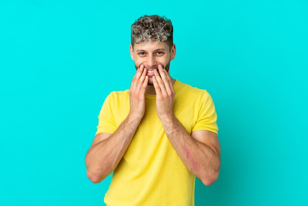 Young handsome caucasian man isolated on blue background happy and smiling covering mouth with hands