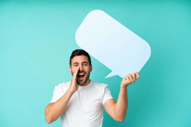 Young handsome caucasian man isolated on blue background holding an empty speech bubble and shouting