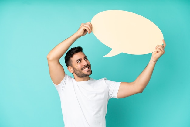 Young handsome caucasian man isolated on blue background holding an empty speech bubble