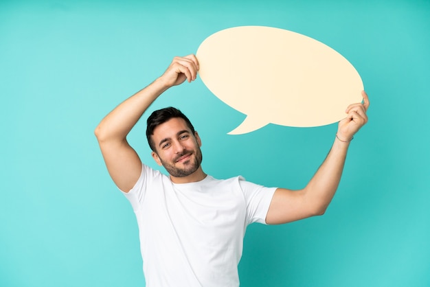 Young handsome caucasian man isolated on blue background holding an empty speech bubble