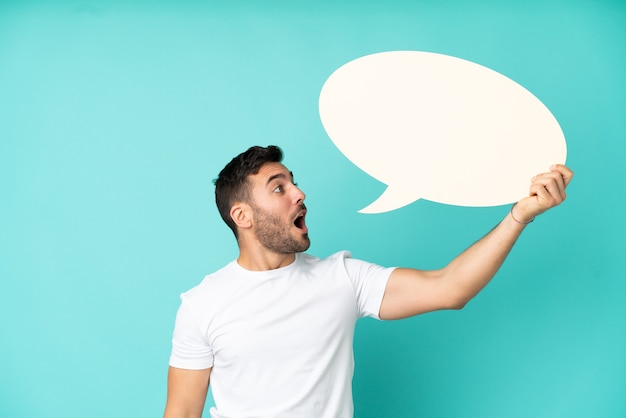 Young handsome caucasian man isolated on blue background holding an empty speech bubble