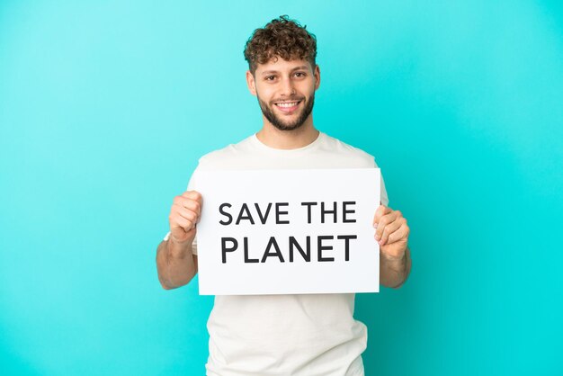 young handsome caucasian man isolated on blue background holding a placard with text save the planet with happy expression