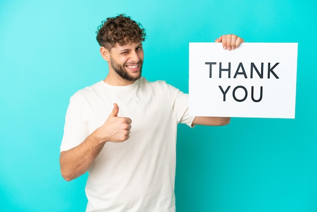 Young handsome caucasian man isolated on blue background holding a placard with text THANK YOU and pointing to the front