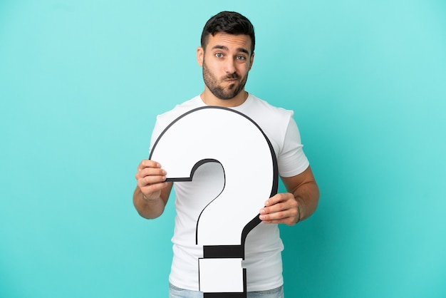 Photo young handsome caucasian man isolated on blue background holding a question mark icon and with sad expression