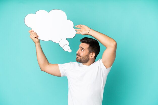 Young handsome caucasian man isolated on blue background holding a thinking speech bubble