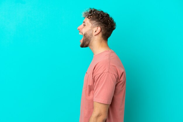 Young handsome caucasian man isolated on blue background laughing in lateral position
