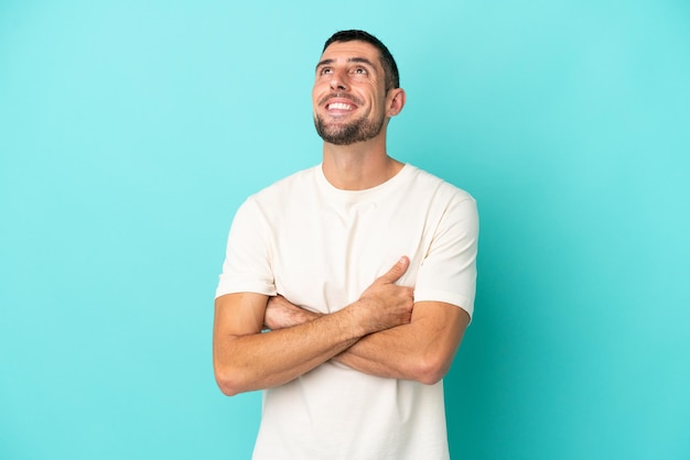 Young handsome caucasian man isolated on blue background looking up while smiling