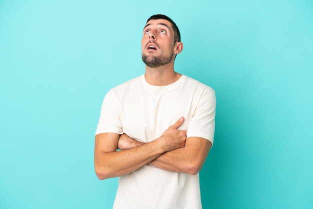 Young handsome caucasian man isolated on blue background looking up and with surprised expression