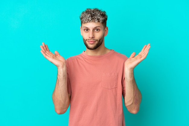 Young handsome caucasian man isolated on blue background making doubts gesture