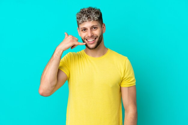 Young handsome caucasian man isolated on blue background making phone gesture. Call me back sign