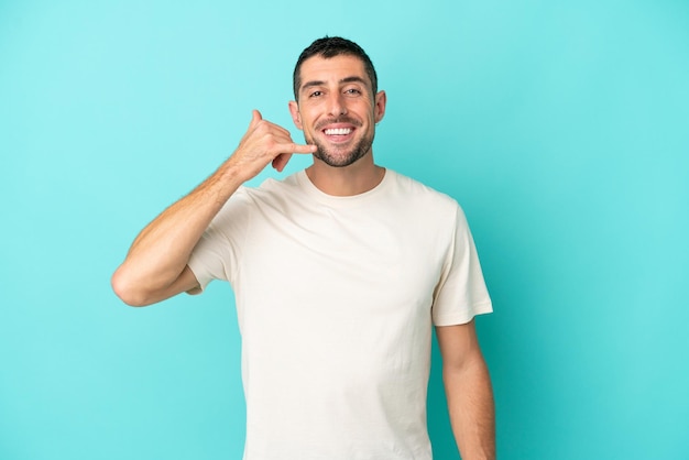 Young handsome caucasian man isolated on blue background making phone gesture Call me back sign