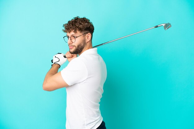 Young handsome caucasian man isolated on blue background playing golf