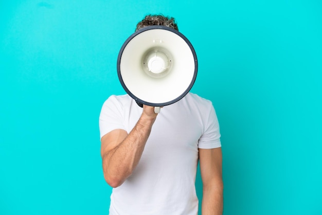 Young handsome caucasian man isolated on blue background shouting through a megaphone to announce something