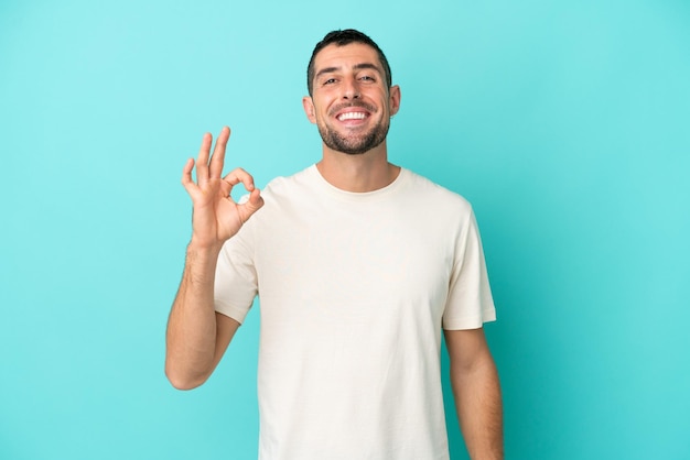 Young handsome caucasian man isolated on blue background showing ok sign with fingers