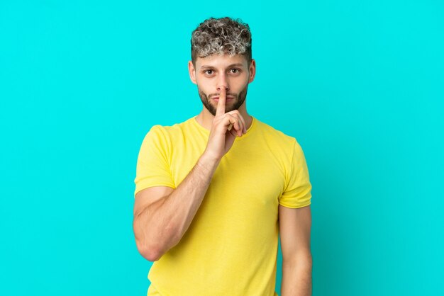 Young handsome caucasian man isolated on blue background showing a sign of silence gesture putting finger in mouth