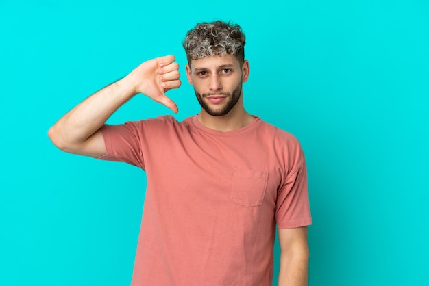 Young handsome caucasian man isolated on blue background showing thumb down with negative expression