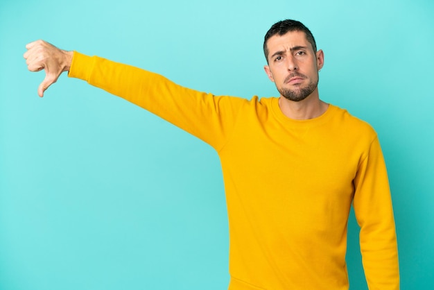 Young handsome caucasian man isolated on blue background showing thumb down with negative expression