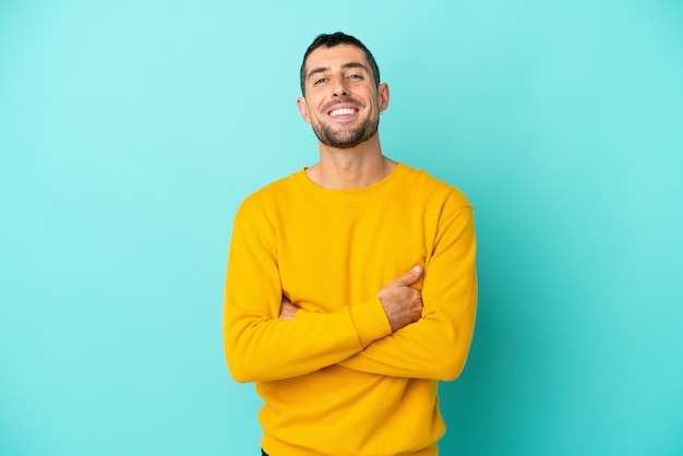 Young handsome caucasian man isolated on blue background with arms crossed and looking forward