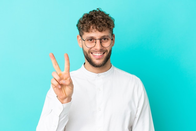 Giovane uomo caucasico bello isolato su sfondo blu con gli occhiali e facendo segno ok