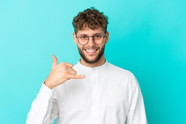 Young handsome caucasian man isolated on blue background With glasses and doing phone gesture