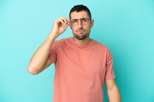 Young handsome caucasian man isolated on blue background With glasses and frustrated expression