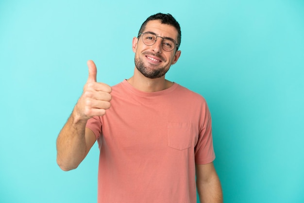 Young handsome caucasian man isolated on blue background With glasses and with thumb up