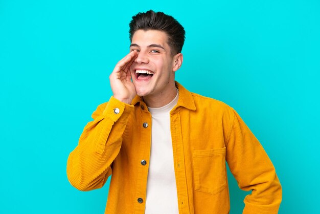 Young handsome caucasian man isolated on blue bakcground shouting with mouth wide open