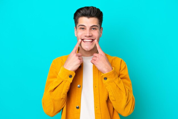 Young handsome caucasian man isolated on blue bakcground smiling with a happy and pleasant expression