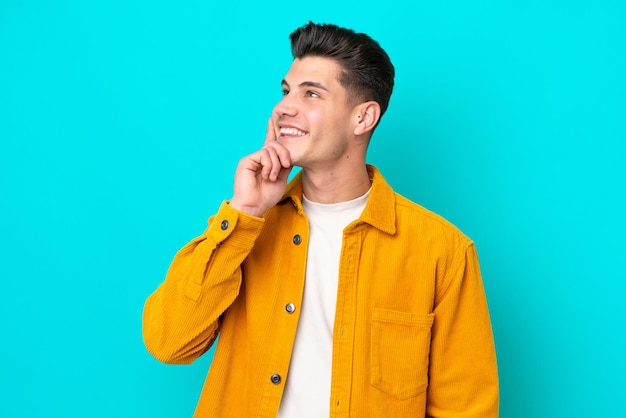 Young handsome caucasian man isolated on blue bakcground thinking an idea while looking up