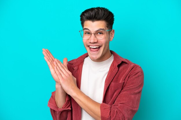 Young handsome caucasian man isolated on blue bakcground With glasses and applauding