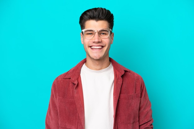 若いハンサムな白人男性は、幸せな表情のメガネで青いbakcgroundに分離