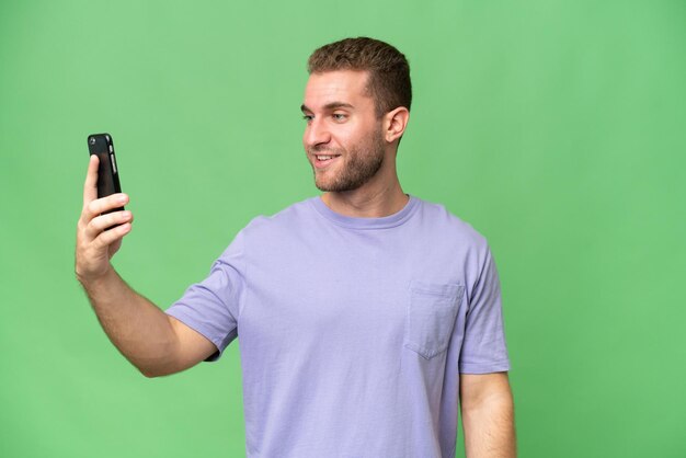 Young handsome caucasian man isolated on green chroma background making a selfie