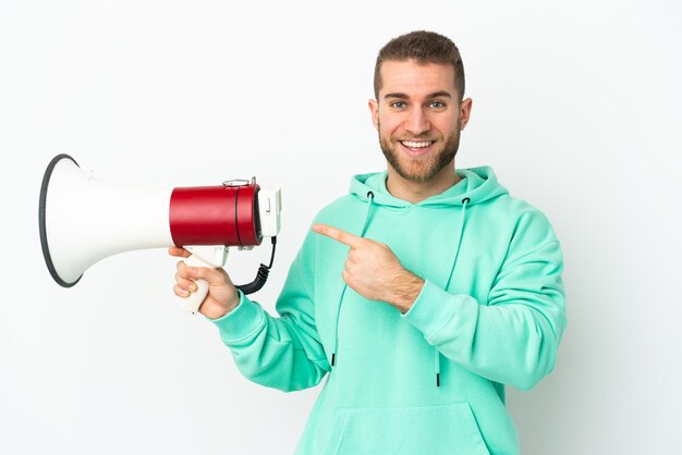 Young handsome caucasian man isolated holding a megaphone and pointing side