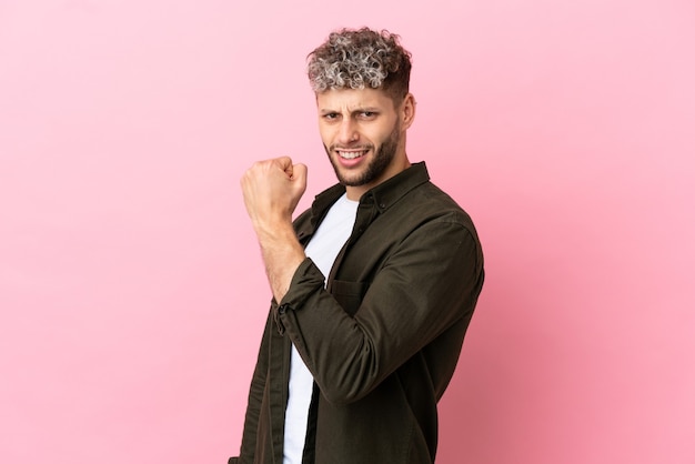 Young handsome caucasian man isolated on pink background celebrating a victory