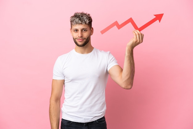 Young handsome caucasian man isolated on pink background holding a catching a rising arrow with happy expression