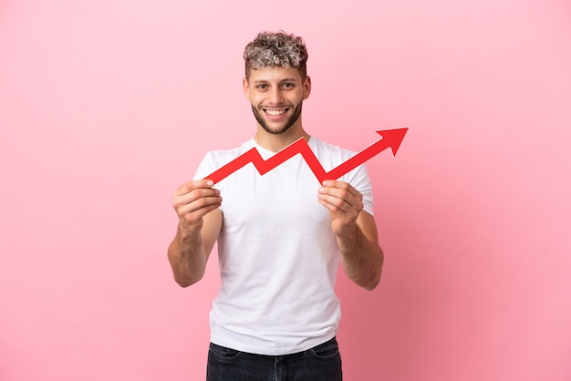 Young handsome caucasian man isolated on pink background holding a catching a rising arrow with happy expression