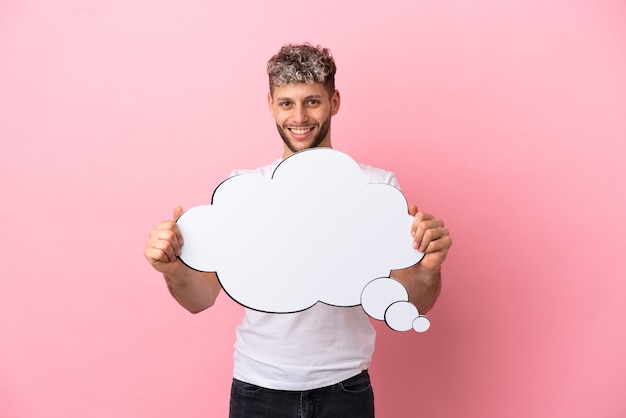 Young handsome caucasian man isolated on pink background holding a thinking speech bubble