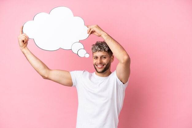 Young handsome caucasian man isolated on pink background holding a thinking speech bubble