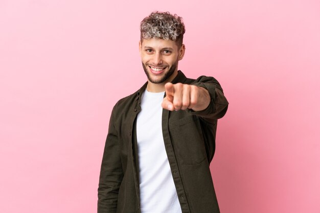 Photo young handsome caucasian man isolated on pink background pointing front with happy expression