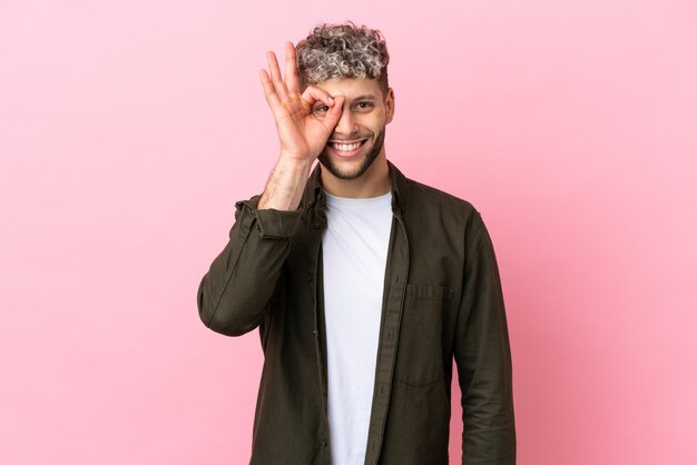 Young handsome caucasian man isolated on pink background showing ok sign with fingers