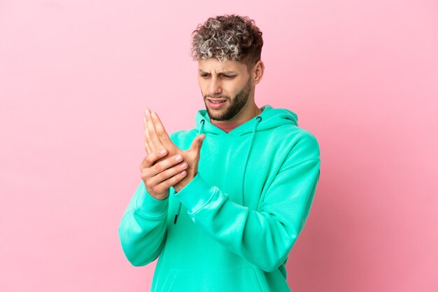 Young handsome caucasian man isolated on pink background suffering from pain in hands